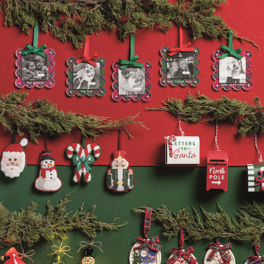 Assorted holiday ornaments including tartan photo frames, nutcrackers, and "Letters to Santa" mailboxes displayed on red.