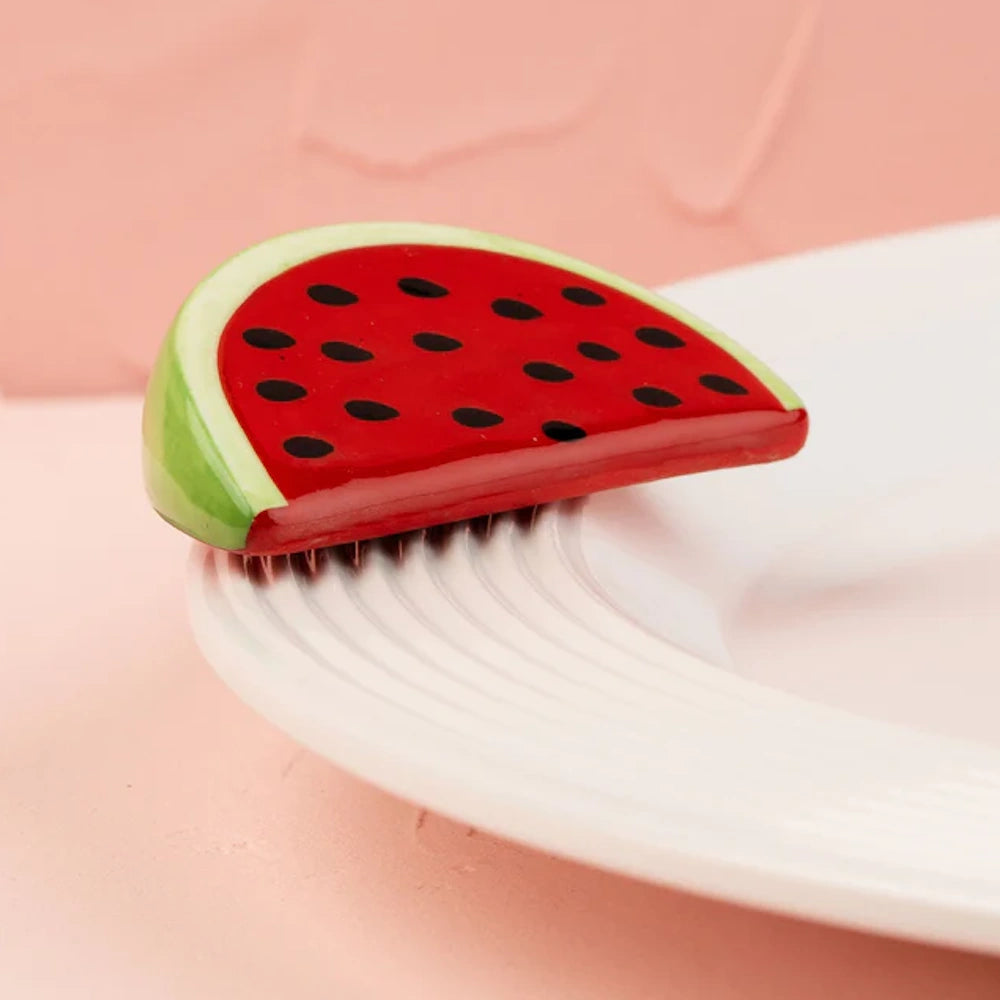 A ceramic watermelon slice decor piece attached to the rim of a white ceramic plate.