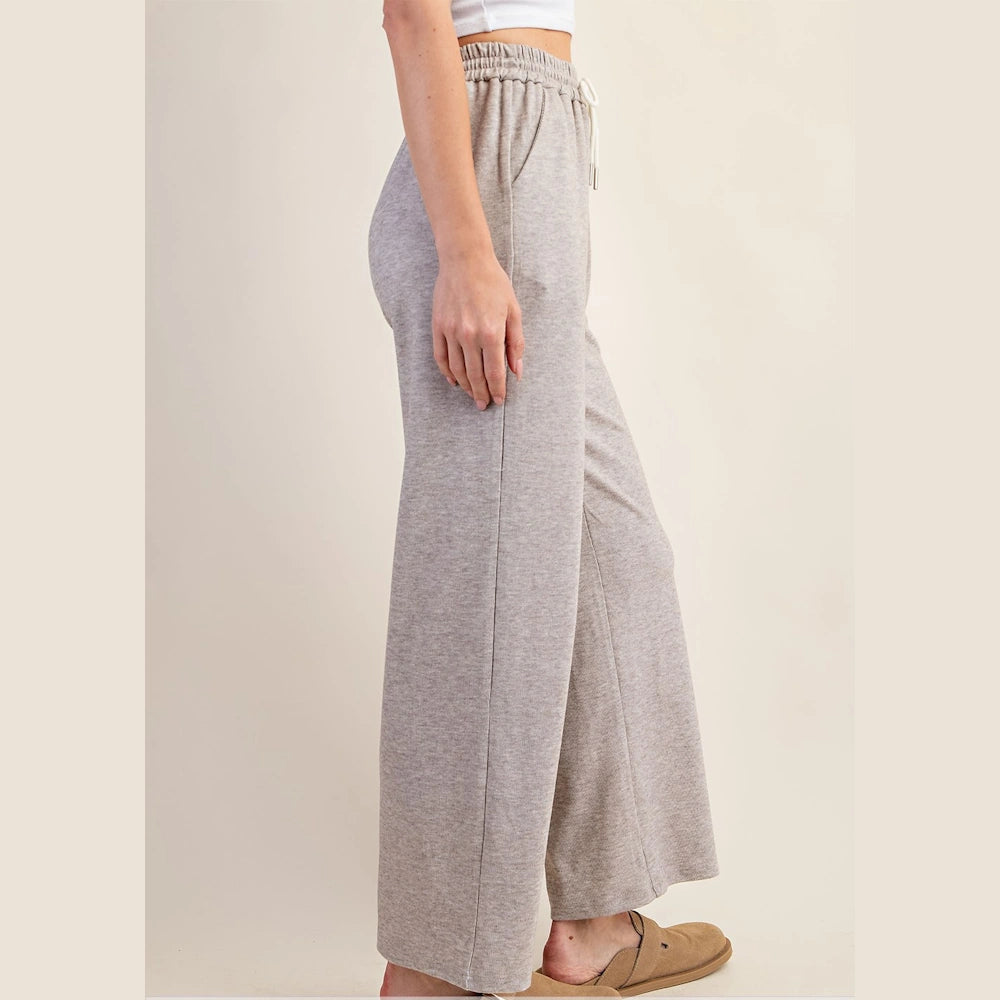 Side view of a person wearing taupe wide-leg knit pants with an elastic drawstring waistband and side pockets.