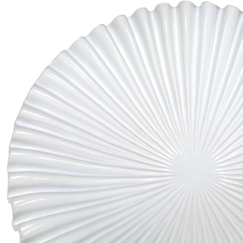 Close-up of a white fluted ceramic plate featuring a textured sunburst pattern and wavy scalloped edges.