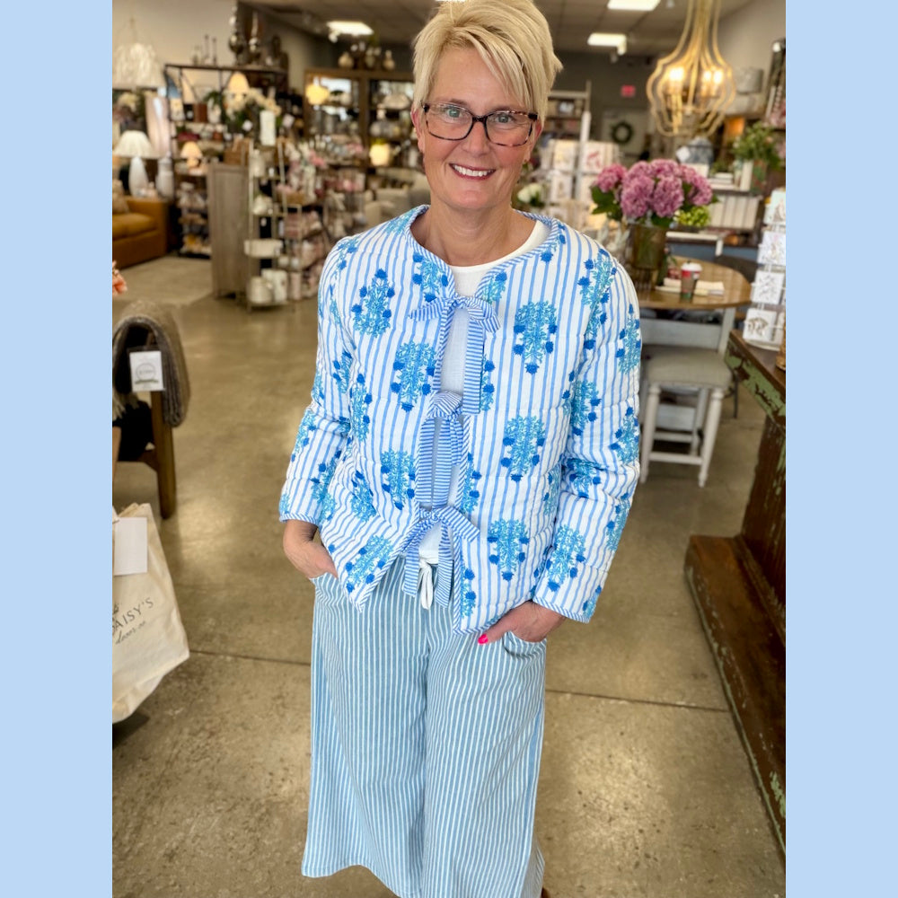 Woman in a blue and white striped quilted jacket with floral embroidery and bow closures posing in a lifestyle boutique.