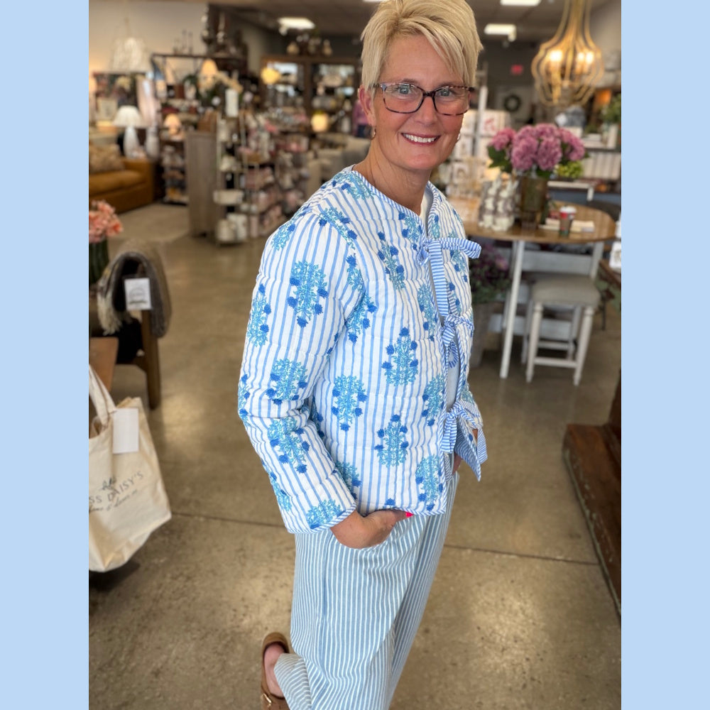 Woman in blue and white striped quilted jacket with floral pattern and bow closures, standing in a boutique store.