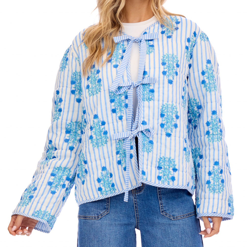Women's blue and white striped quilted jacket with floral print and front bow ties, styled with denim jeans.