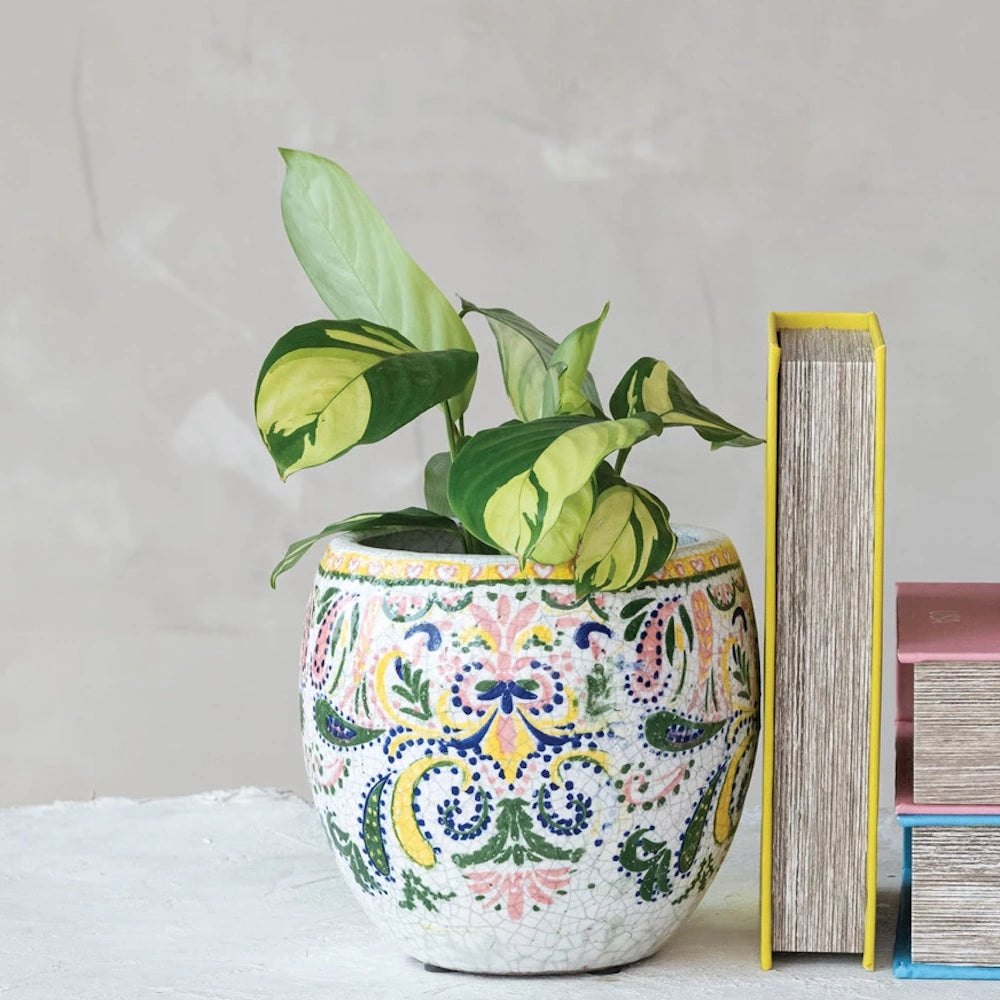Small houseplant in a decorative mosaic-style planter with colorful bohemian patterns on a desk.