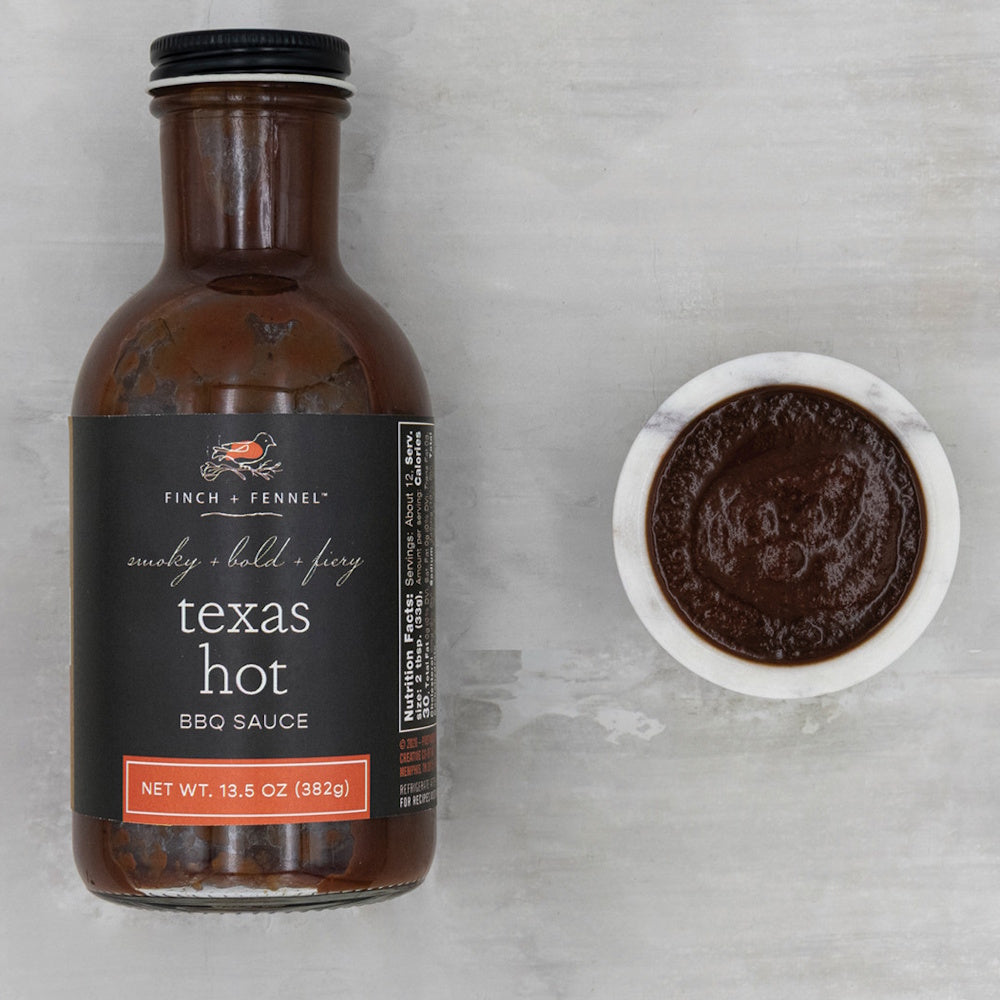 A bottle of Finch & Fennel Texas hot BBQ sauce next to a small marble bowl of dark sauce, top-down view.