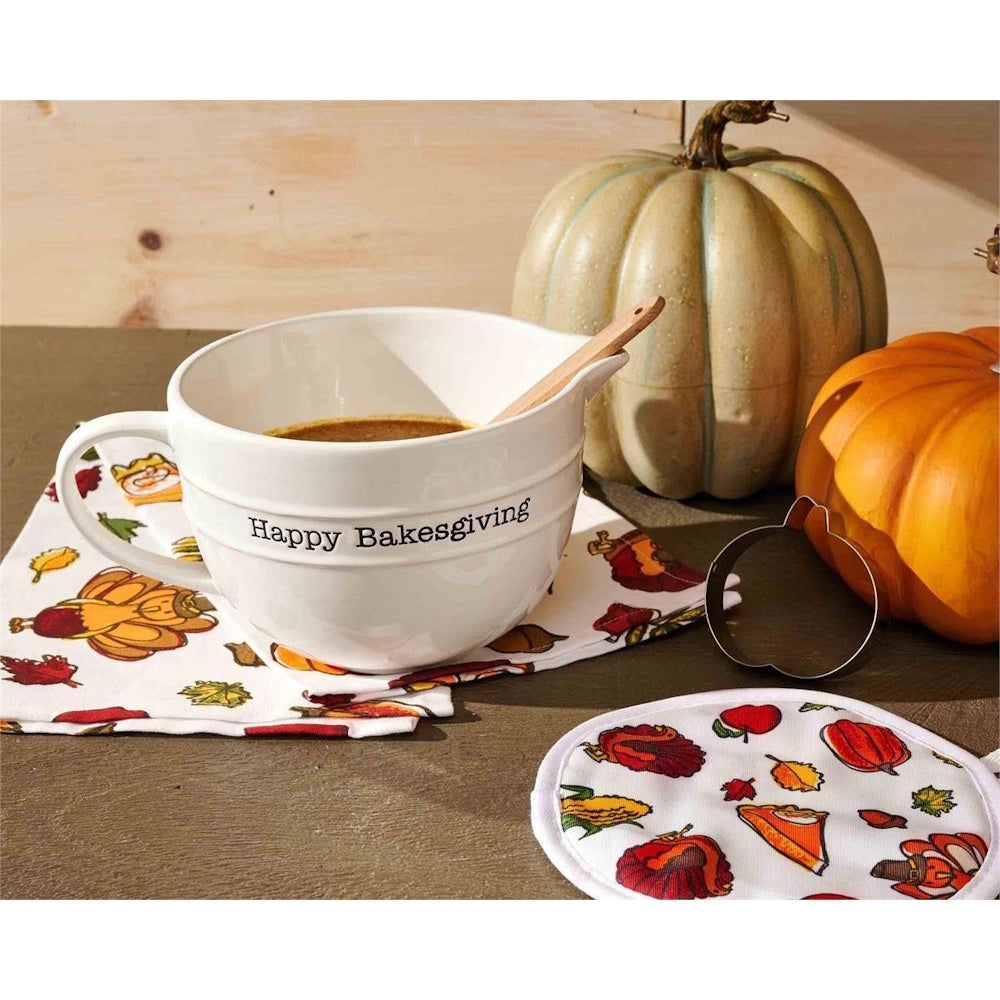 White ceramic mixing bowl reading "Happy Bakesgiving" displayed with pumpkins and fall decor.