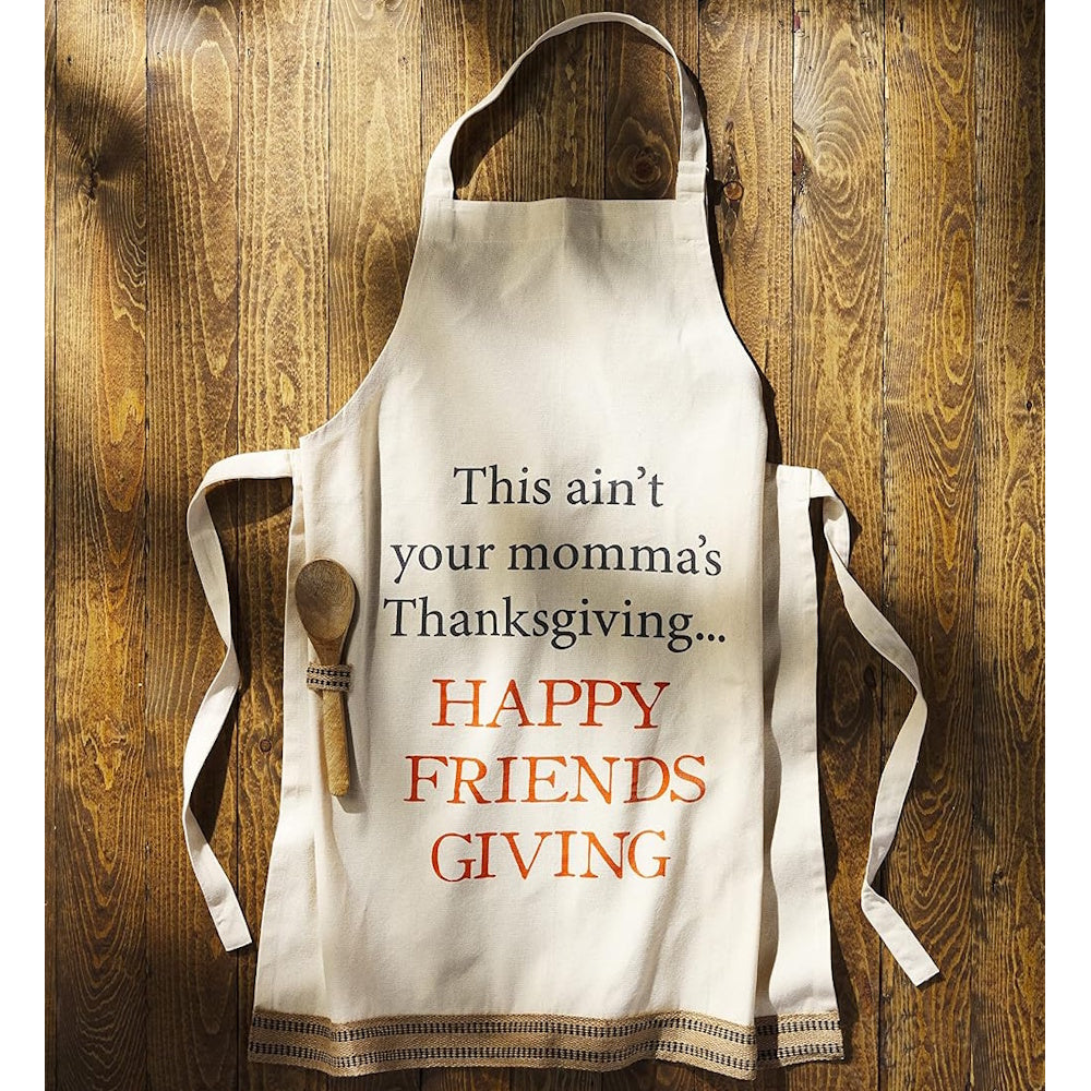 Beige apron with "Happy Friendsgiving" text and a wooden spoon displayed on a rustic wood surface.