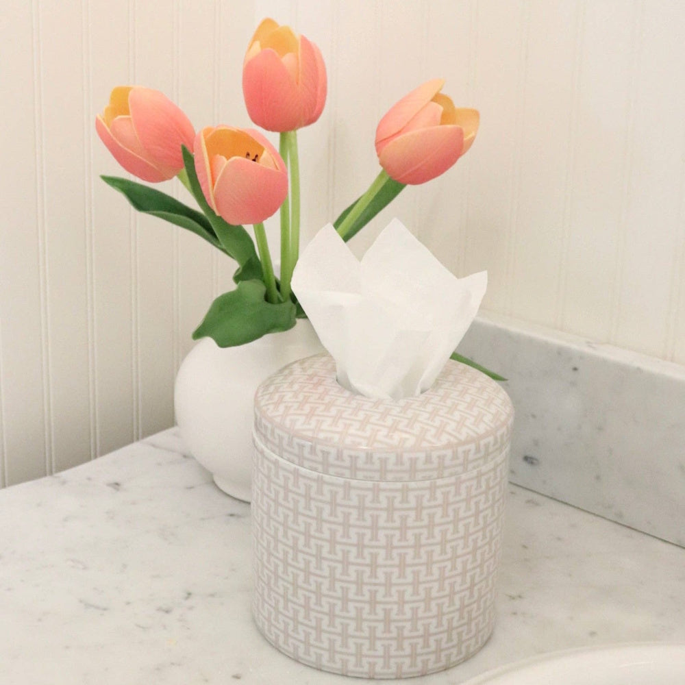 Geometric-patterned tissue vessel on a marble countertop beside a white vase with pink tulips.