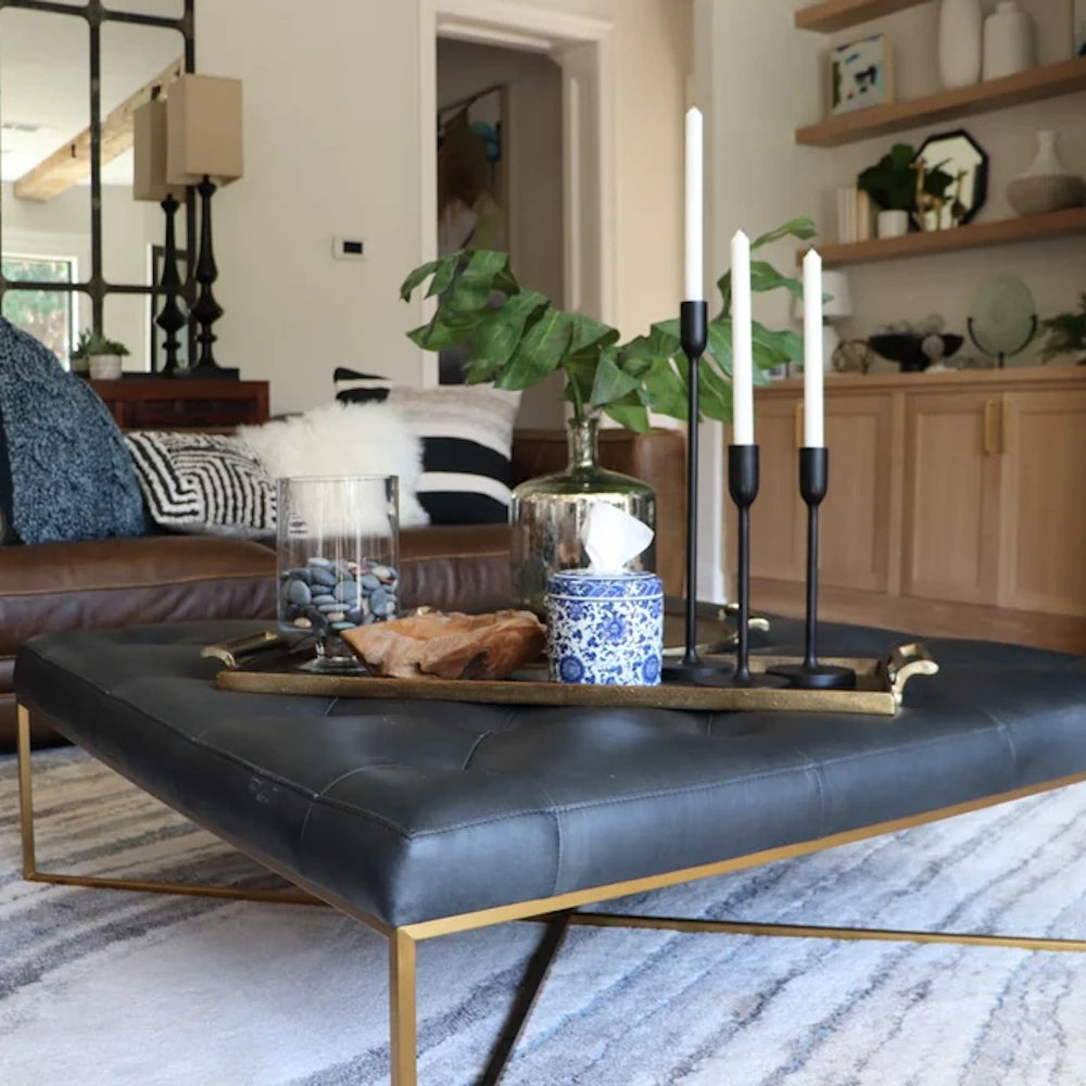 Tufted black leather coffee table with gold legs, a tray of decor including Chinoiserie blue & white tissue box, and candle holders.