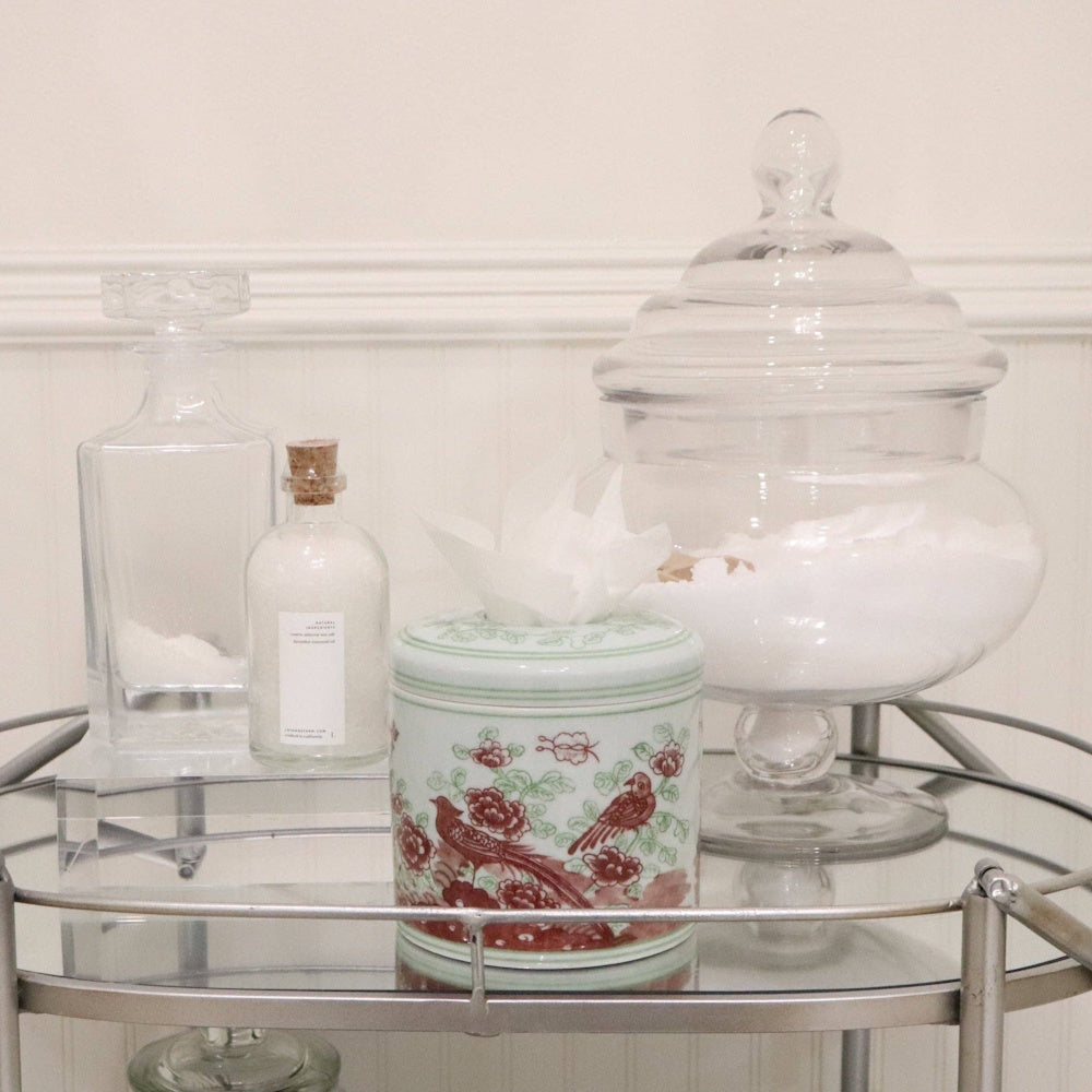 Porcelain tissue vessel with floral and bird pattern on a bar cart with glass jars.