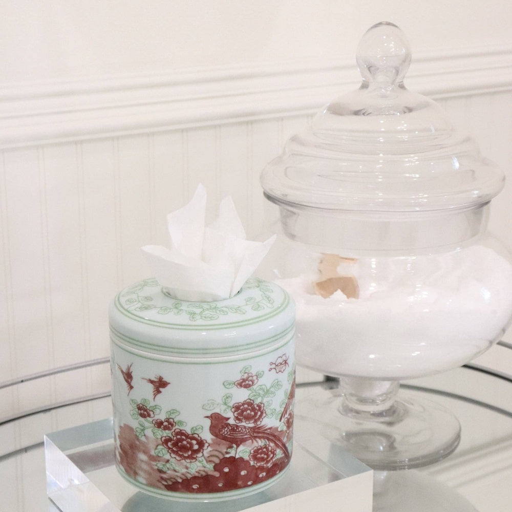 Porcelain tissue vessel with floral and bird pattern next to a glass jar.