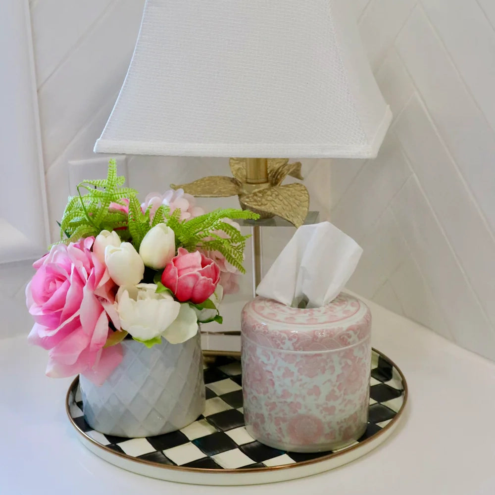 Pink floral tissue canister and rose bouquet on a checkered tray beside a gold leaf lamp with a white shade.