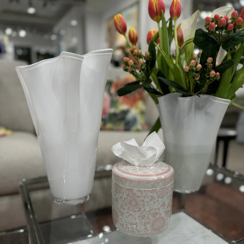 Pink floral tissue jar and two wavy white glass vases with red tulips and berries on a glass table.