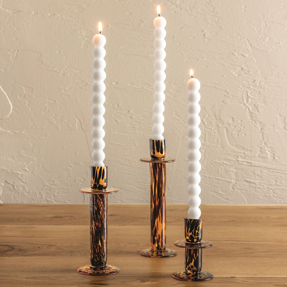 Trio of tortoiseshell glass taper candle holders in varying heights with lit white bubble candles on a wooden table.