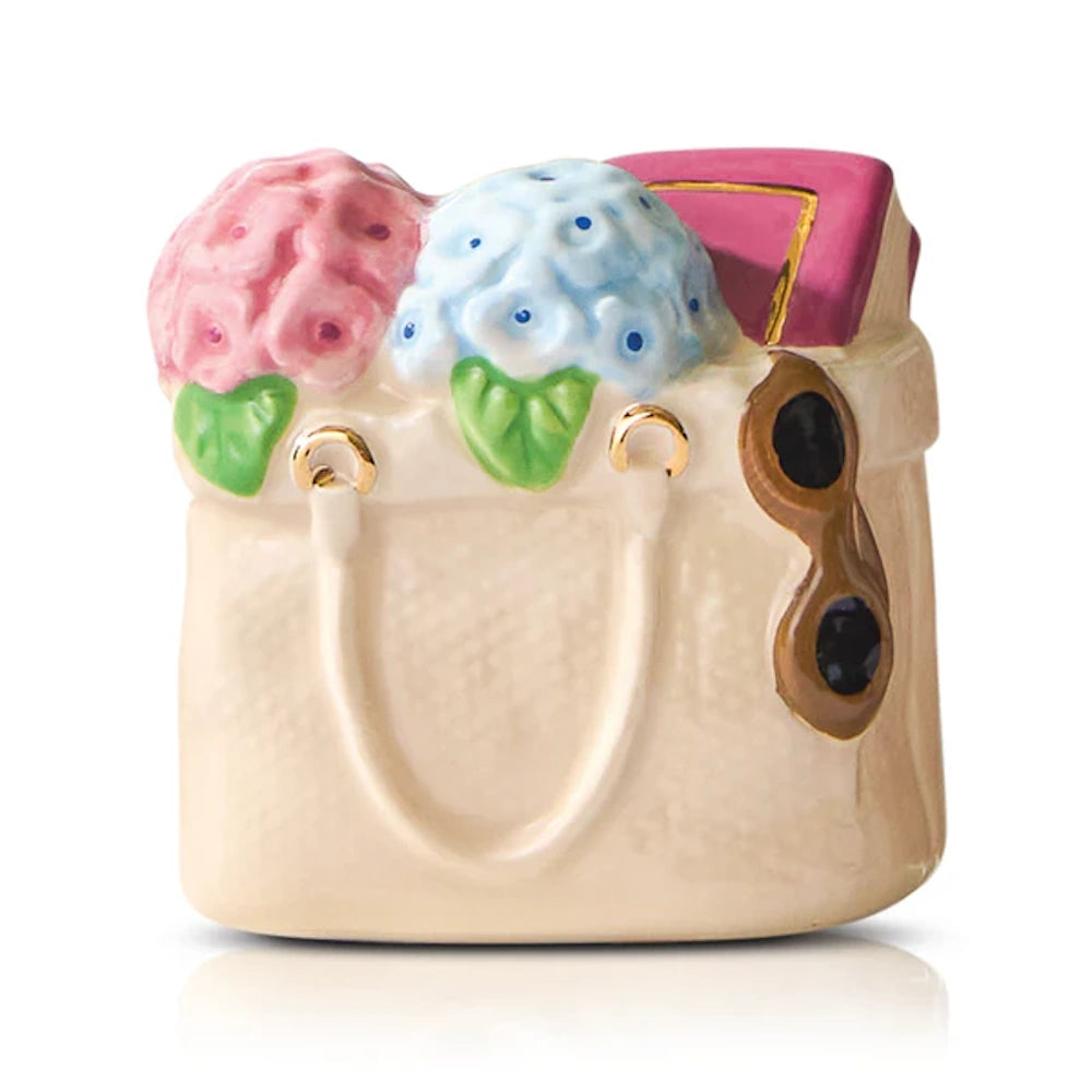 Ceramic tote bag figurine with pink and blue flowers, a pink book, and sunglasses on a white background.