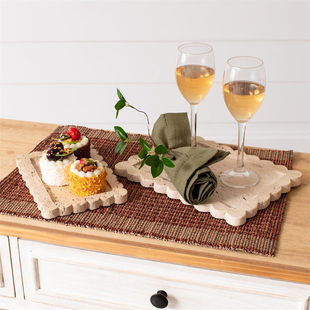 Scalloped travertine stone trays holding desserts and wine glasses on a woven placemat for elegant home decor.