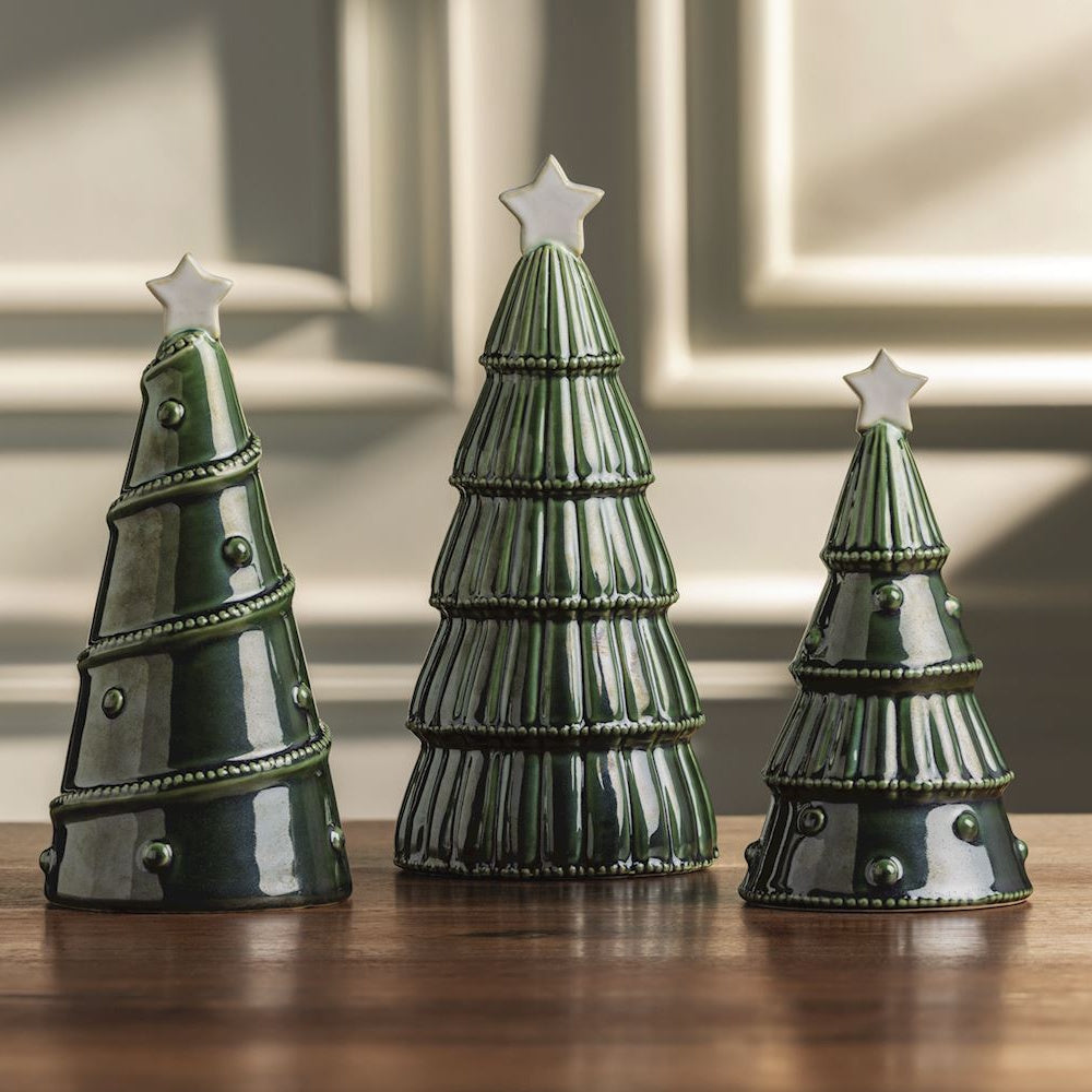 Three green ceramic Christmas tree tabletop figurines with white stars on top.