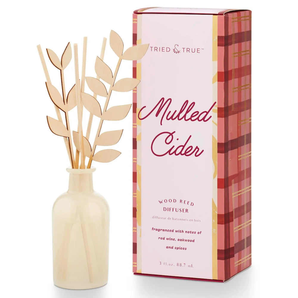 Tried & True Mulled Cider reed diffuser with leaf-shaped wooden reeds next to its plaid pink box.