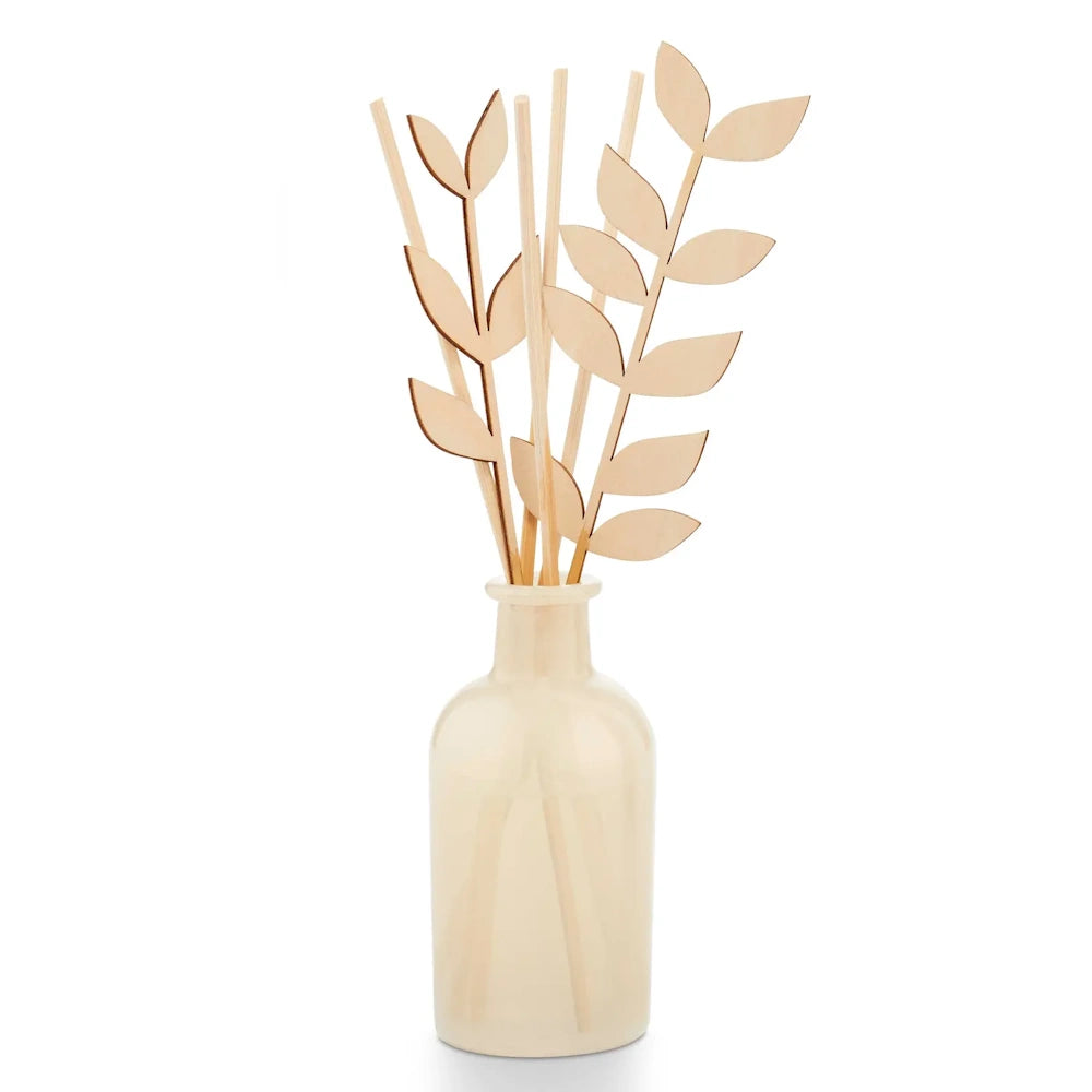 A cream-colored glass diffuser bottle with wooden reeds and leaf-shaped wooden sticks against a white background.
