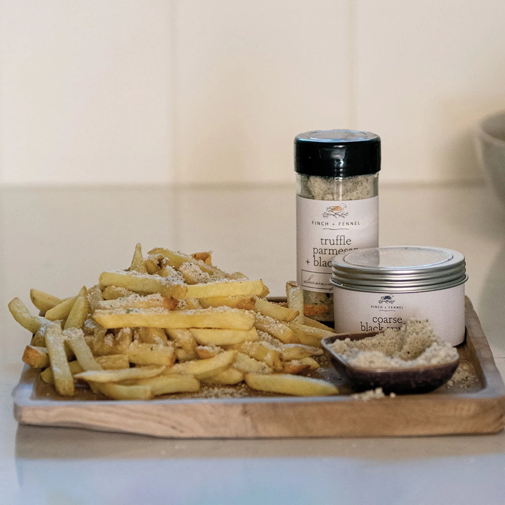 French fries seasoned with Finch + Fennel Truffle Parmesan + Black Garlic Seasoning on a wooden board.