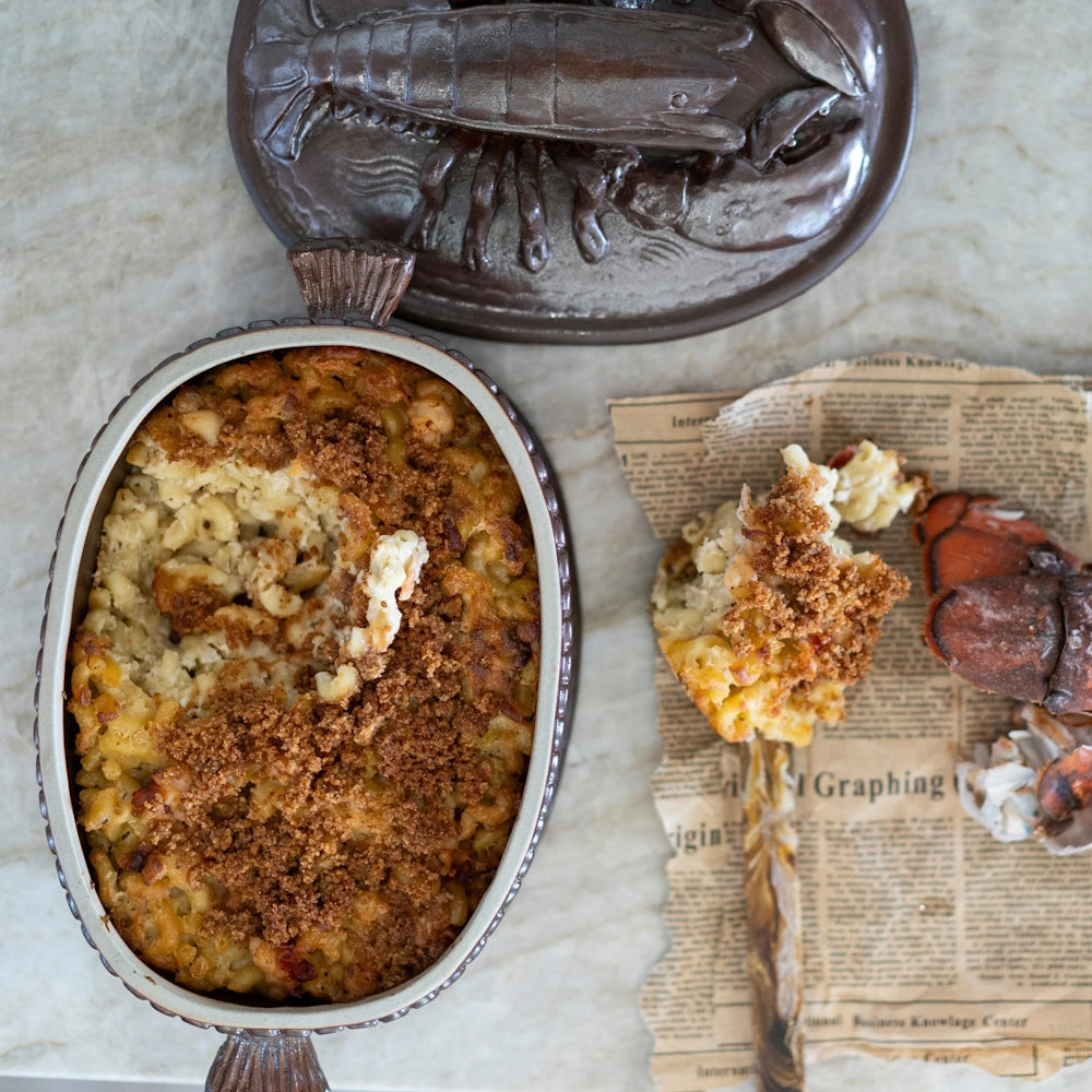 Baked lobster mac and cheese topped with a crispy breadcrumb crust in an oval dish alongside a lobster claw.