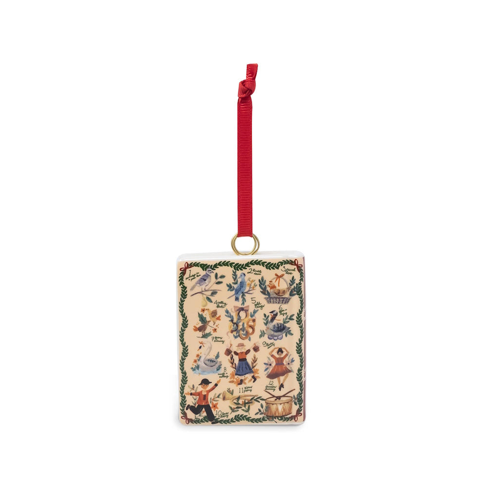 Ceramic book ornament illustrating the Twelve Days of Christmas gifts, suspended by a red ribbon.