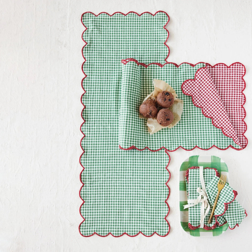 Green gingham table runner styled on a white surface with baked goods and matching scalloped napkins.
