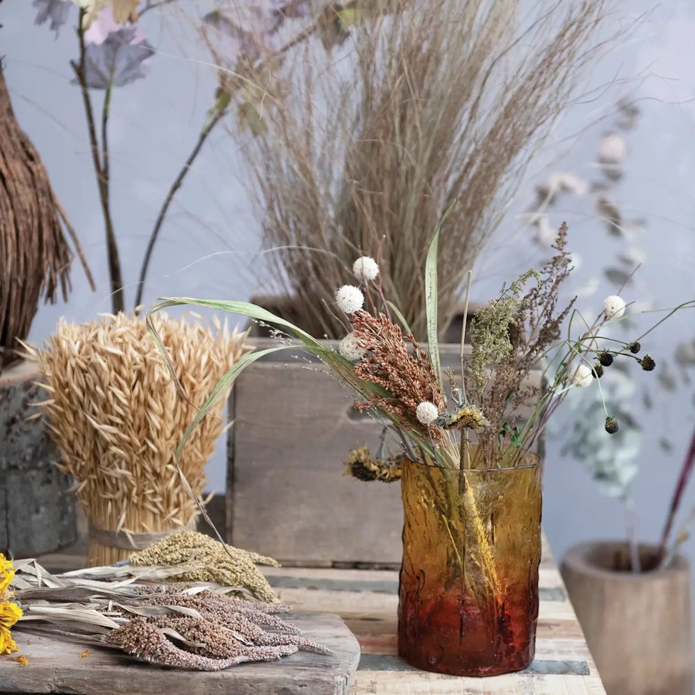 A textured, two-tone amber glass vase filled with dried botanicals on a rustic tabletop.