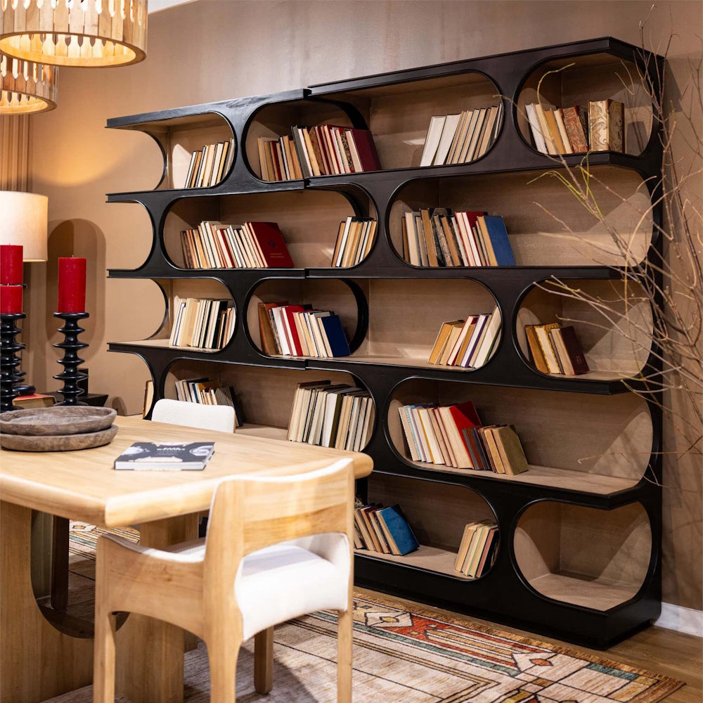 Modern black crescent cutout bookcase filled with books behind a wooden dining table.