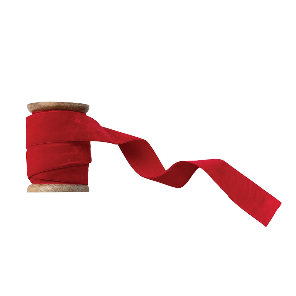 Red velvet ribbon wrapped around a rustic wooden spool with an unspooled tail.