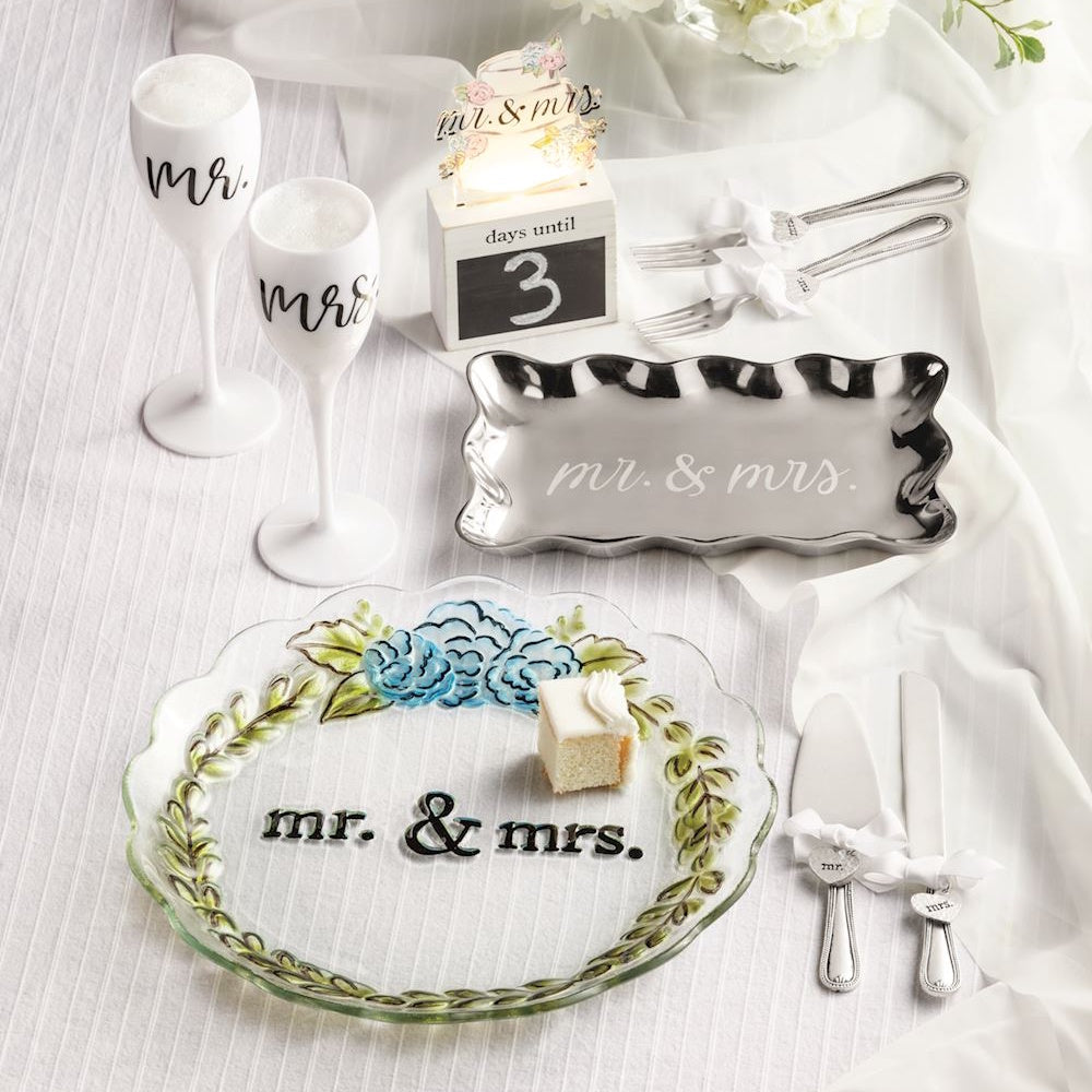 Mr. and Mrs. wedding cake serving set including glass plate, silver tray, forks, and champagne flutes with floral accents.
