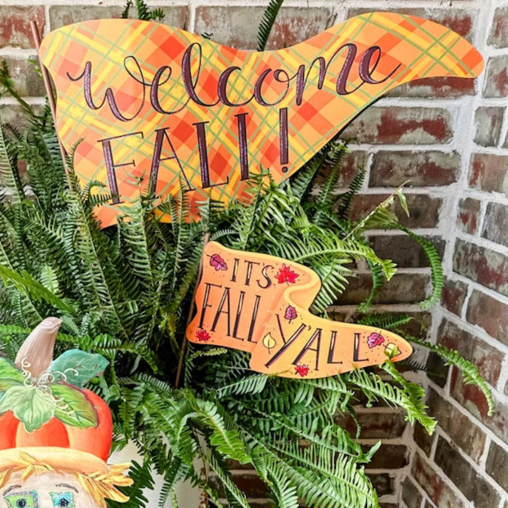 Scarecrow and pumpkin decor next to a fern with plaid Welcome Fall and Its Fall Yall yard signs.