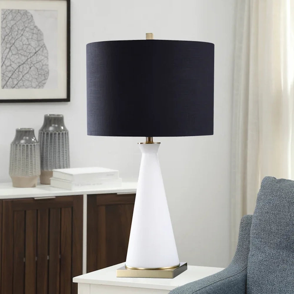Modern table lamp featuring a white conical glass base, brass accents, and a large navy blue drum shade.