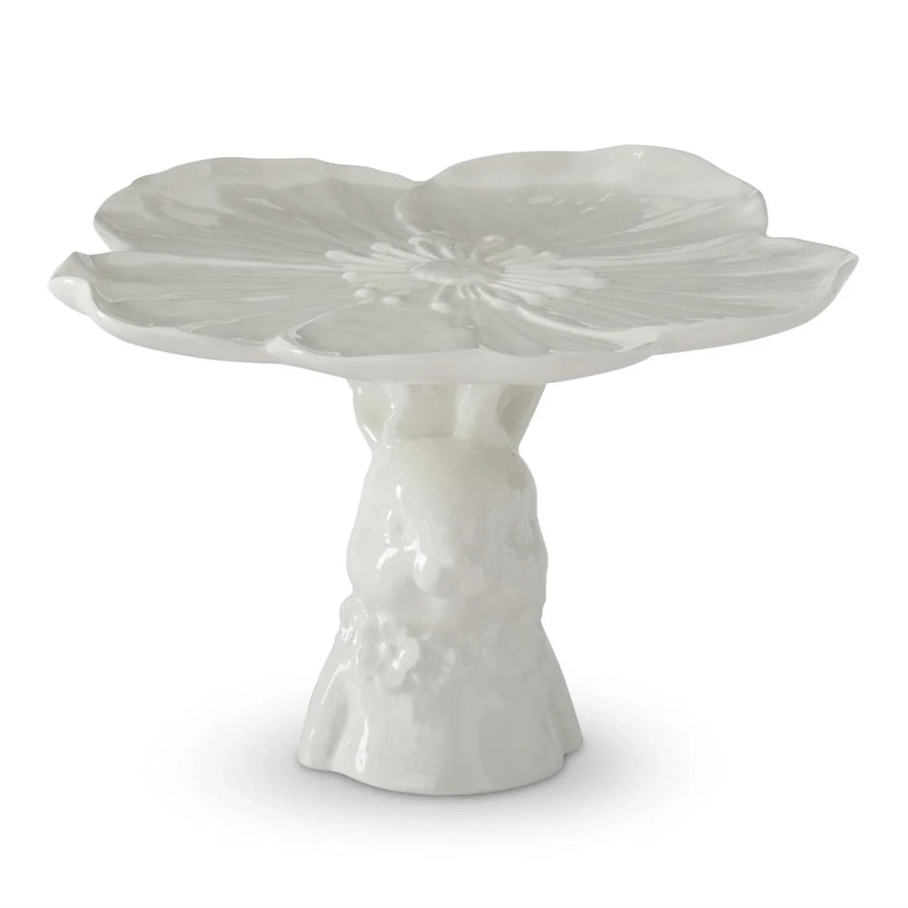 A white ceramic cake stand with a flower-shaped platter supported by a bunny figurine pedestal base.