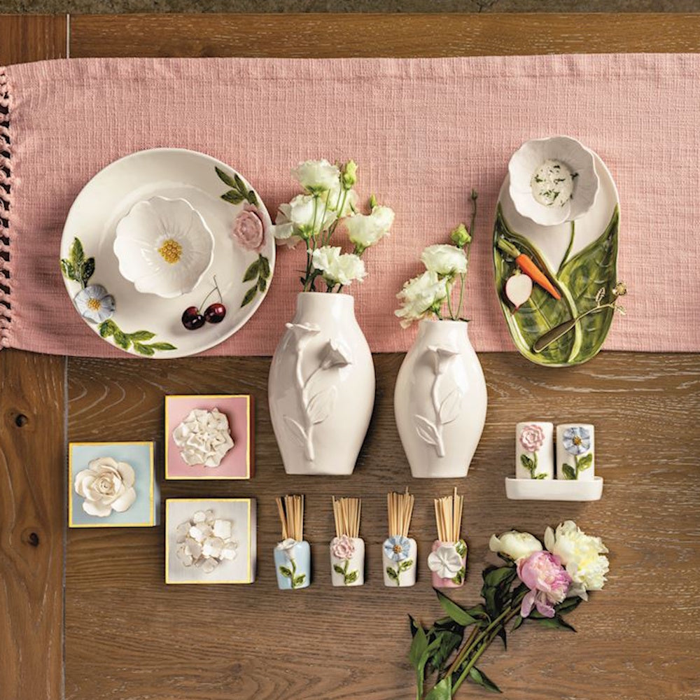 White ceramic floral vases, plates, and decor with 3D flower accents on a wooden table with a pink runner.