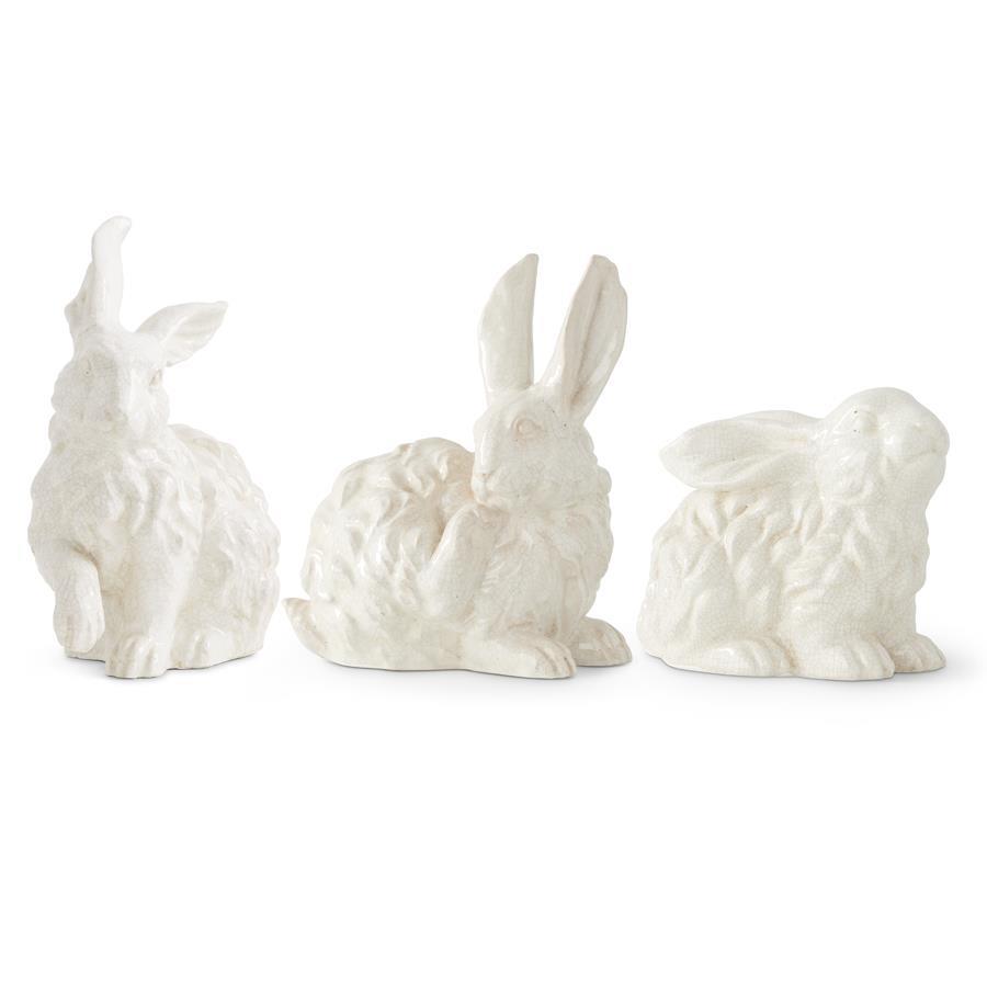 Three white glazed terracotta bunny figurines in various sitting and grooming poses on a white background.