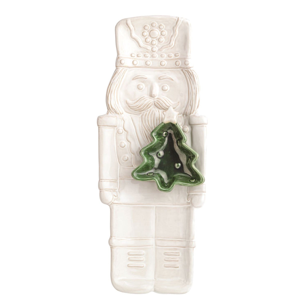 White ceramic nutcracker serving platter holding a small green Christmas tree dip bowl.