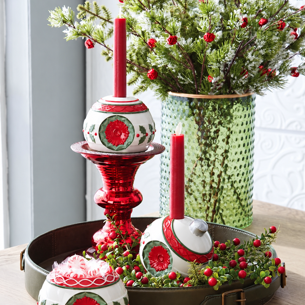 Holiday display featuring ornament taper candleholders with red candles on a tray with greenery and a vase.