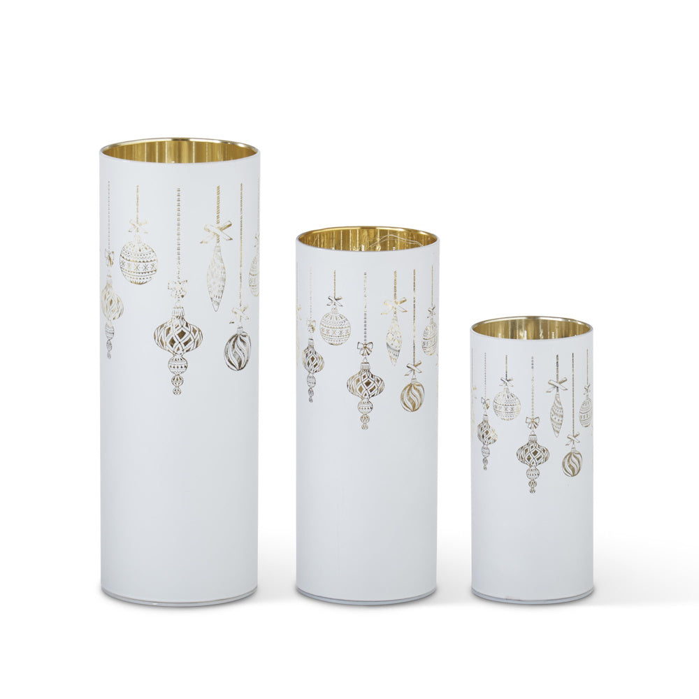 Set of three white metallic cylinders in varying sizes adorned with hanging gold ornament laser-engraved designs.