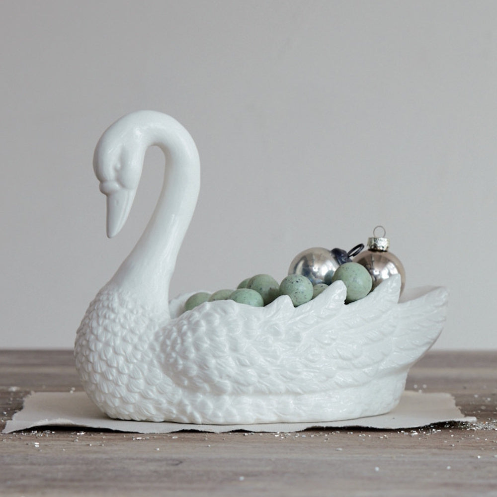 White ceramic swan-shaped decorative dish filled with green beads and mini ornaments.