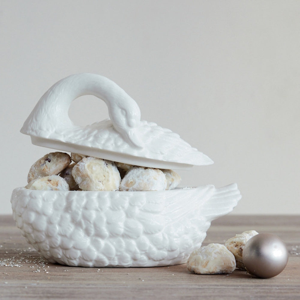 White swan-shaped lidded jar partially open to reveal treats, resting on a wooden surface.