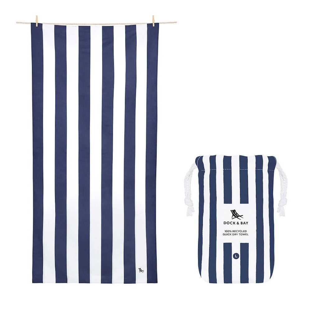 A large, blue and white vertically striped beach towel hanging next to its matching drawstring pouch.