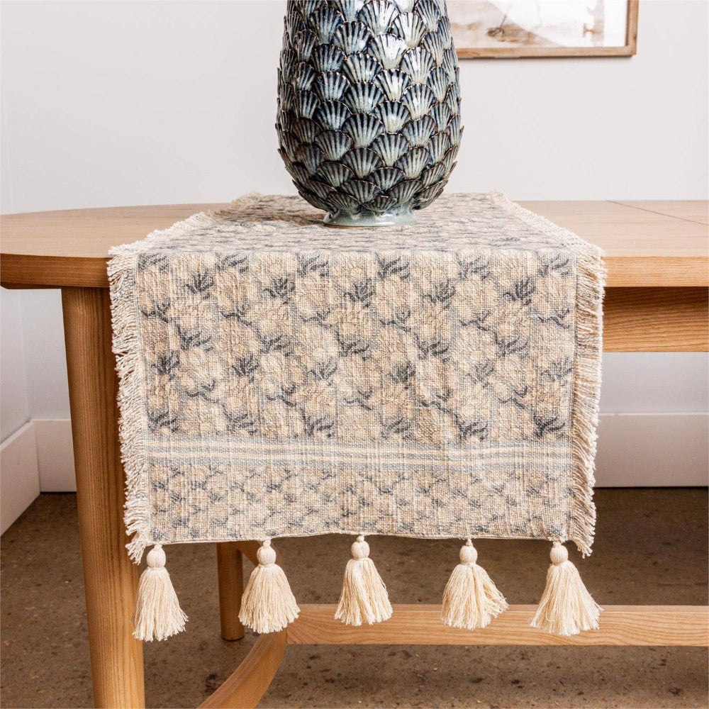 Windward blue block print table runner with fringe and tassels on a light wood dining table with a decorative vase.