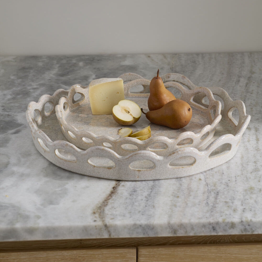 Two speckled ceramic trays nested together on marble, holding a wedge of cheese and bosc pears.