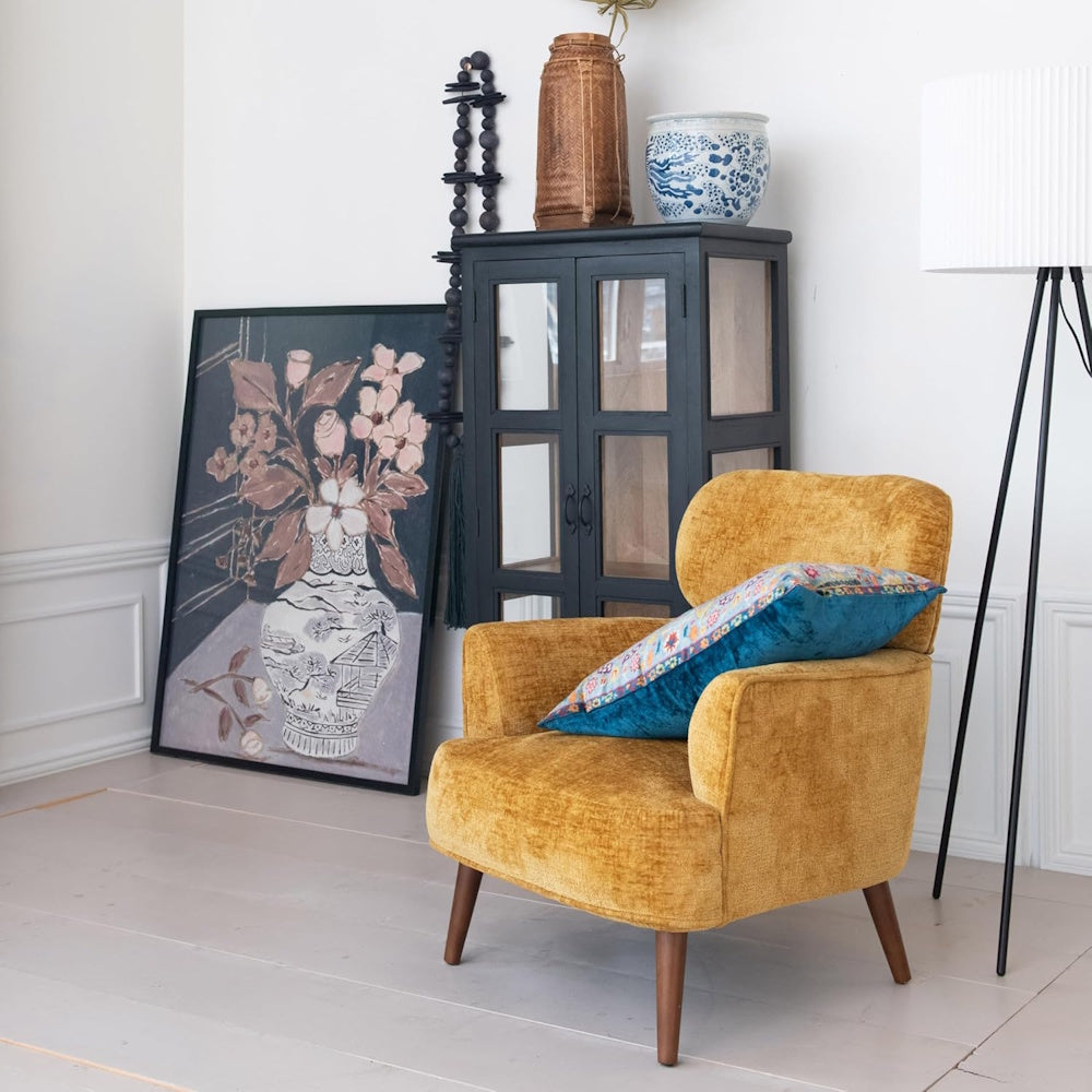 Wood-framed glass wall decor featuring a floral painting leaned against a wall in a bright, modern living room setting.