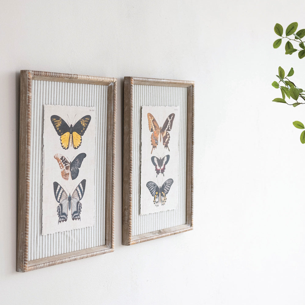 Two wood-framed wall art pieces featuring vintage butterfly illustrations on striped mats against a white wall.