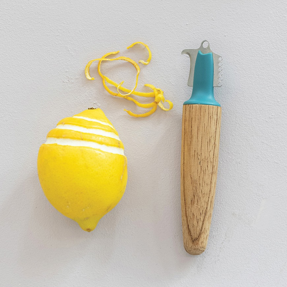 Wooden citrus zester tool beside a partially zested lemon and lemon peel curls on a light background.