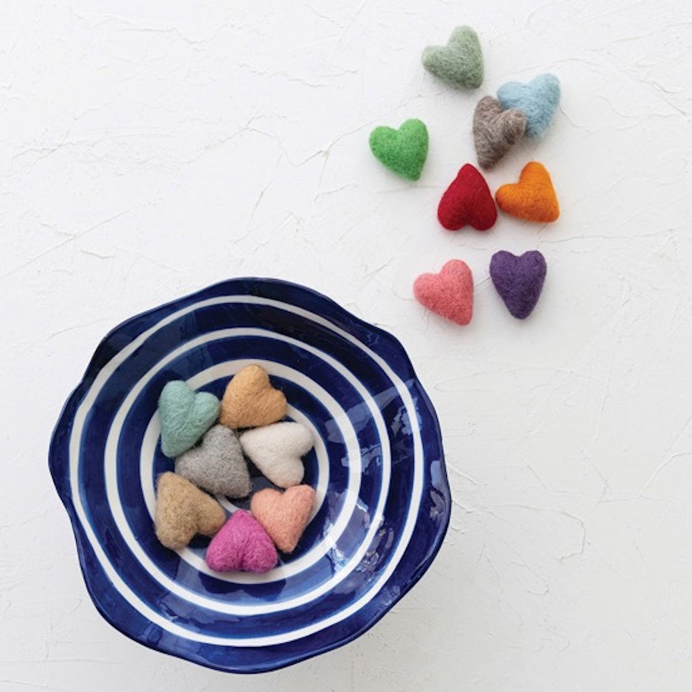 A blue and white striped bowl filled with colorful felt hearts, with more felt hearts scattered on a white surface.