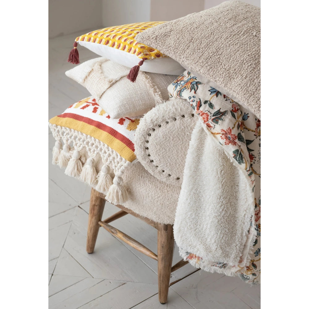 Assorted decorative pillows and a plush throw blanket with fringe and tassel details in a neutral, modern room.