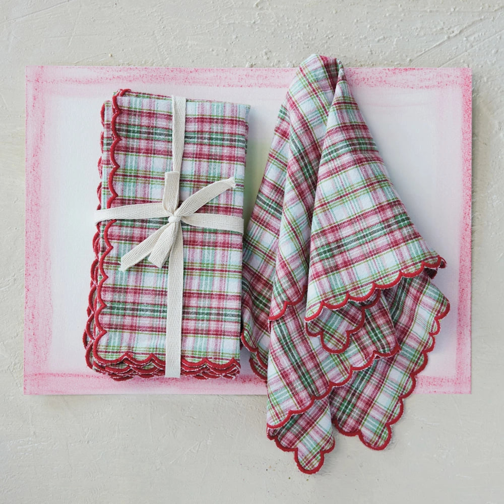 Red and green plaid napkins with scalloped edges, shown folded with a ribbon and draped on a pink-bordered mat.